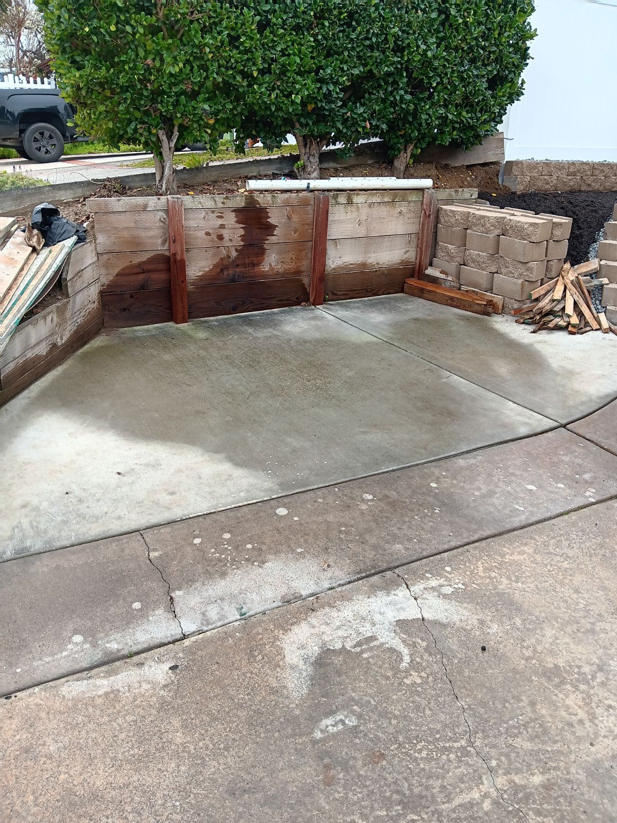 Concrete patio with retaining wall, trees, and debris.
