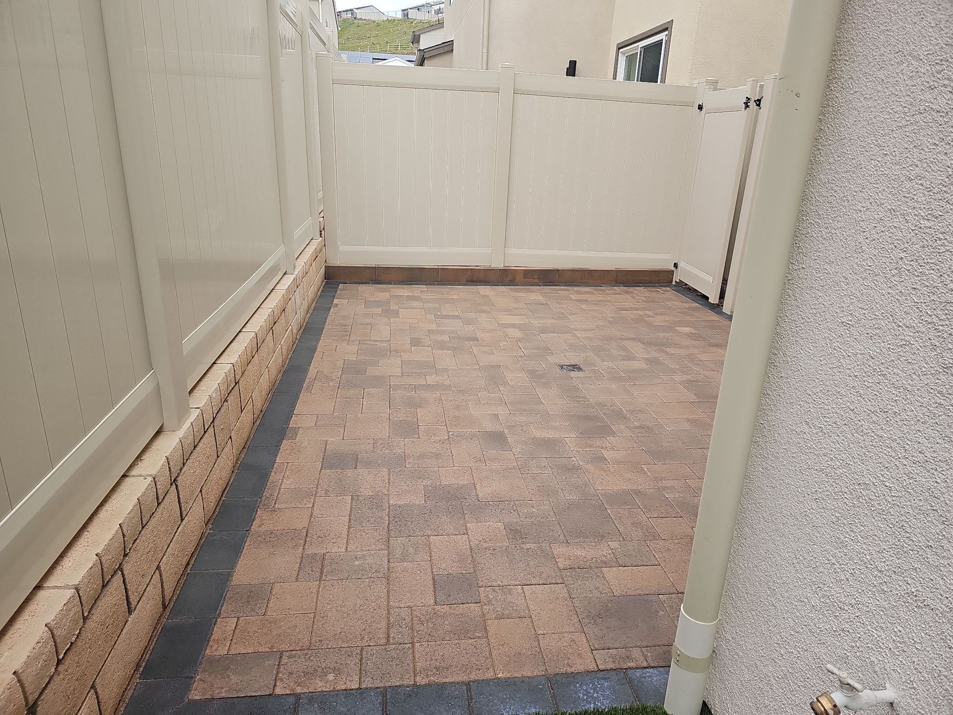 Small brick-paved patio enclosed by beige vinyl fencing and a light beige exterior wall.