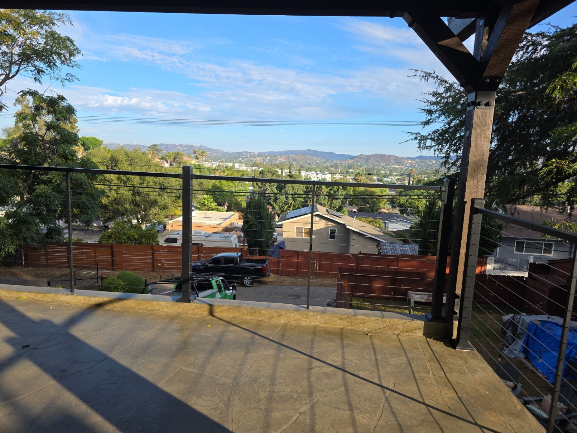 Patio overlooking a cityscape with black railing and overcast sky. Shadow on concrete.