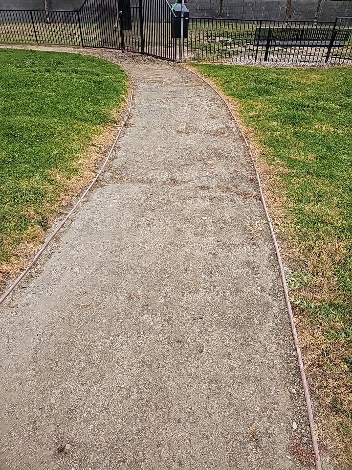 A gravel path curves through green grass toward a gate in a park.