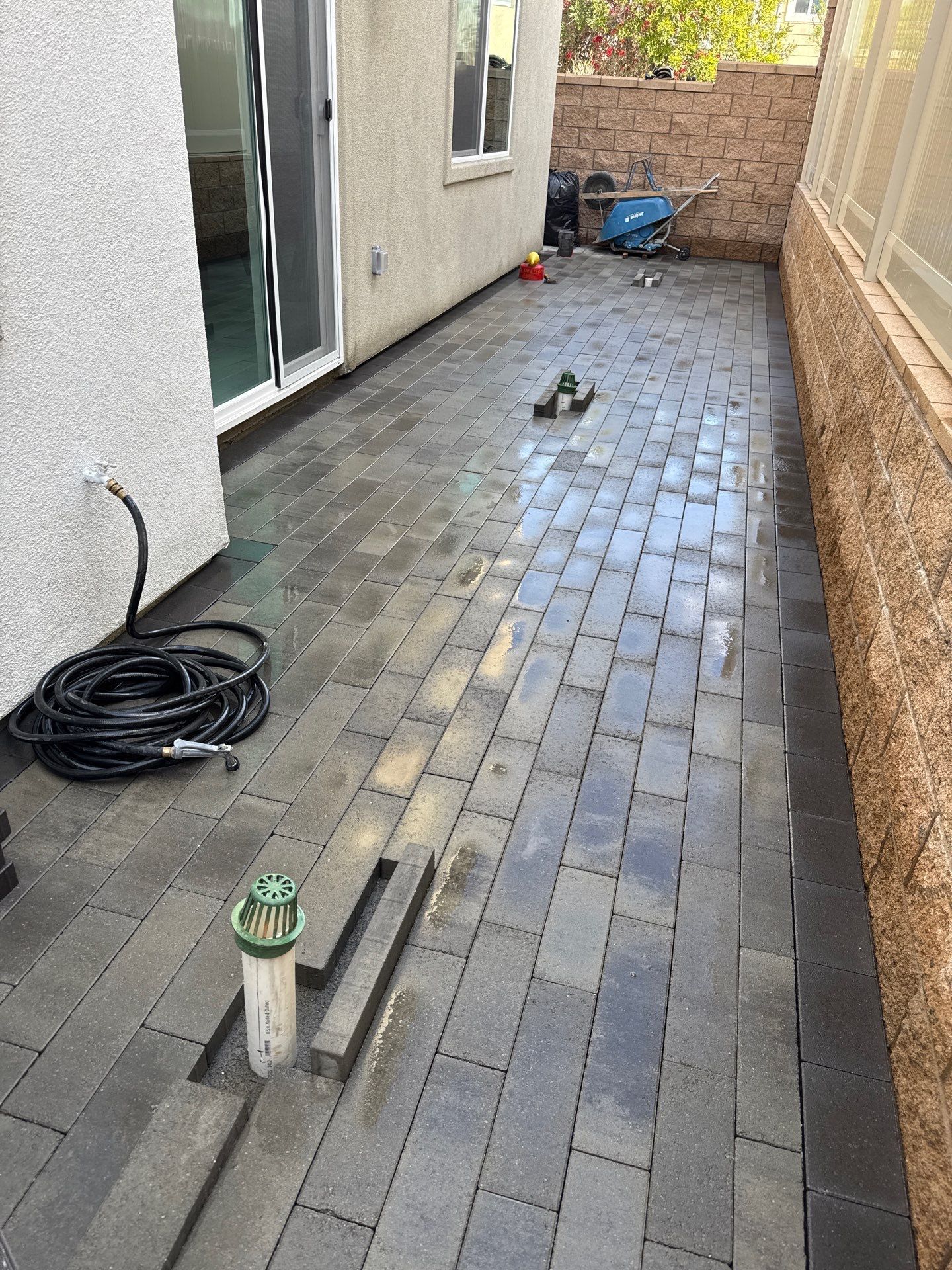 Brick patio with black pavers, next to a house with a sliding glass door and a low wall.