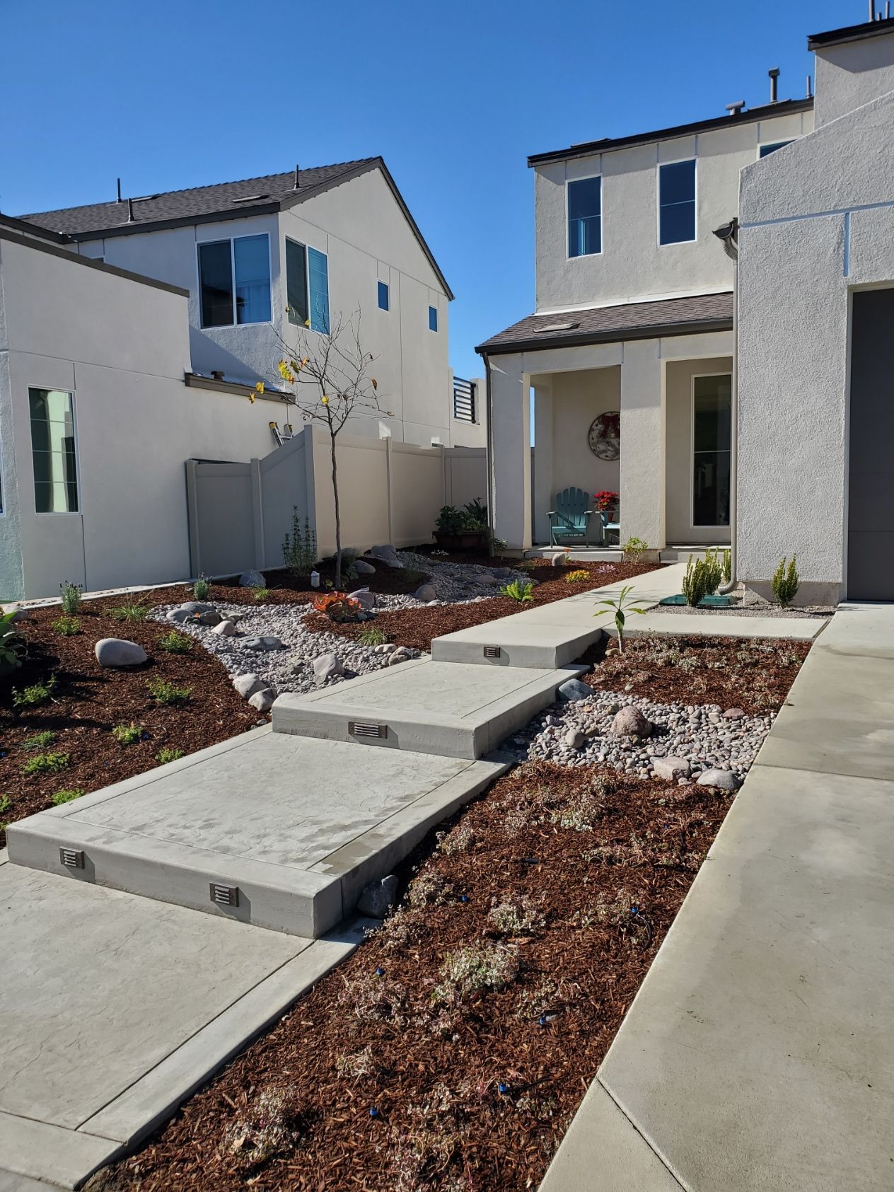 Concrete steps lead to a light-colored house with a small front yard of mulch and rocks.