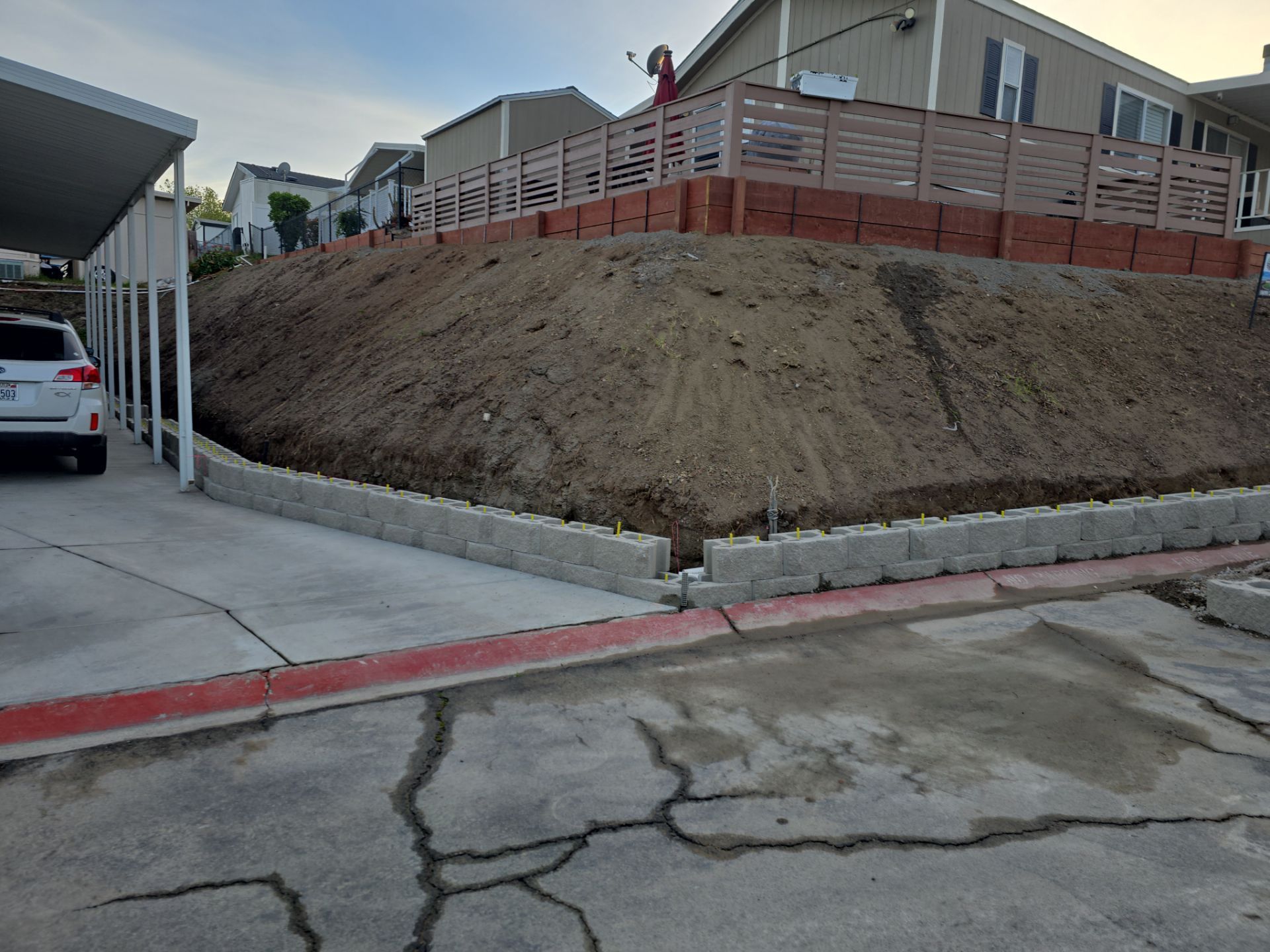 A dirt hillside with retaining walls. A car is parked on the left. A person is standing on the top.