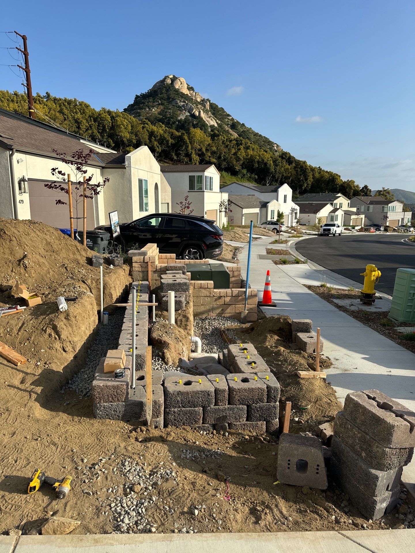 Construction site with retaining wall being built on a residential street; mountain in background.