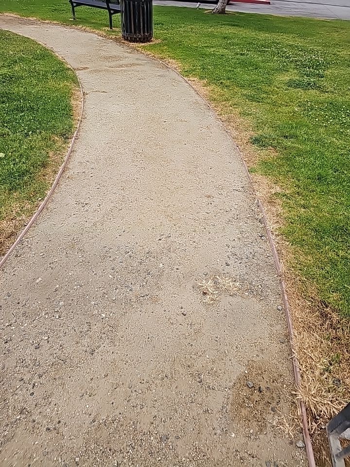 Curved gravel path in a park, bordered by green grass and a metal edge.