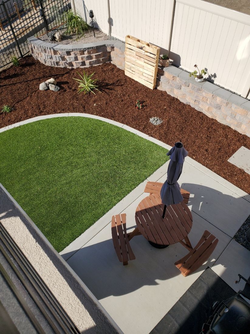 Backyard with green turf, patio, and raised garden beds with brown mulch.