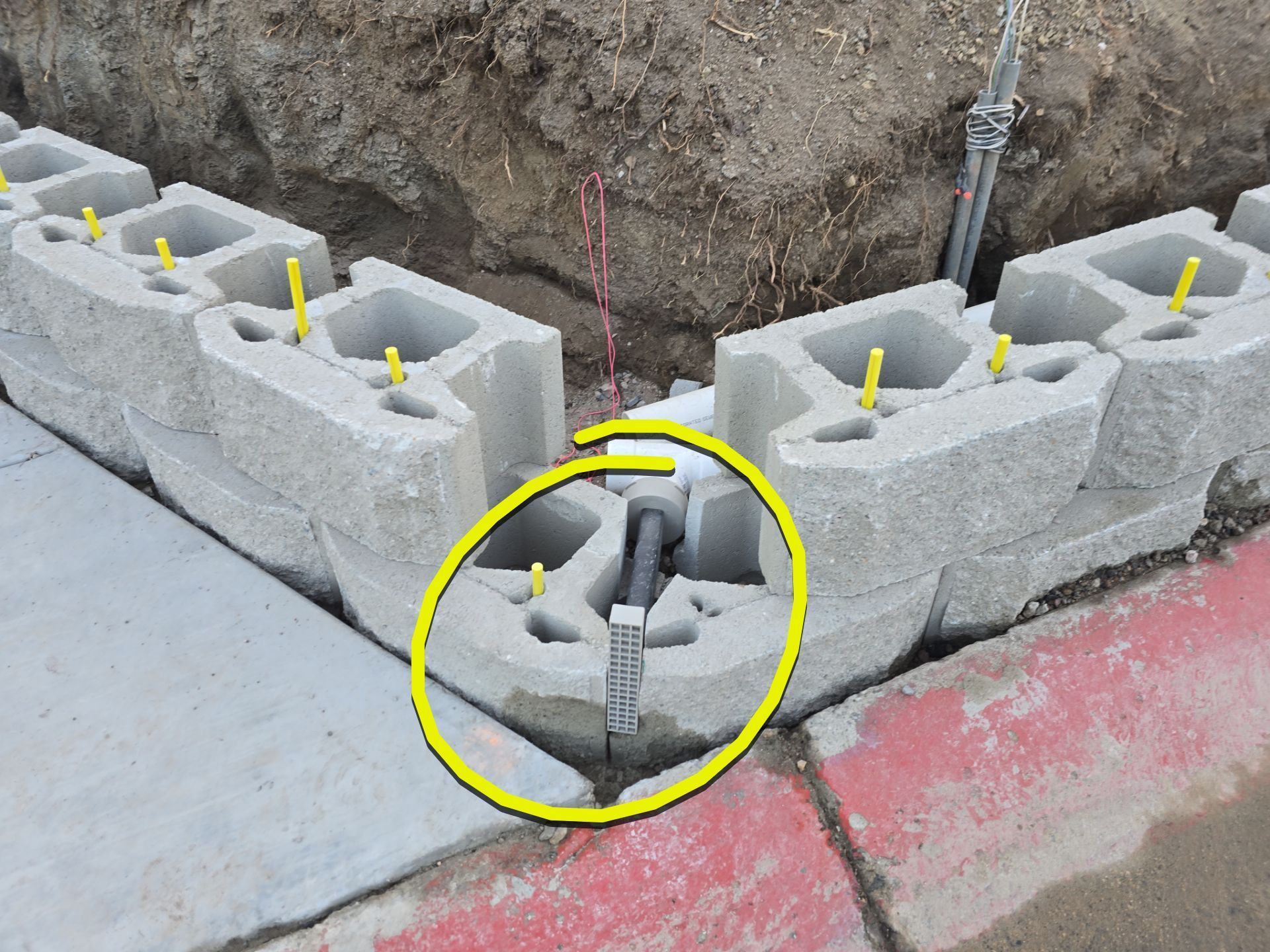 Concrete block retaining wall under construction at a street corner, with drainage pipe visible.