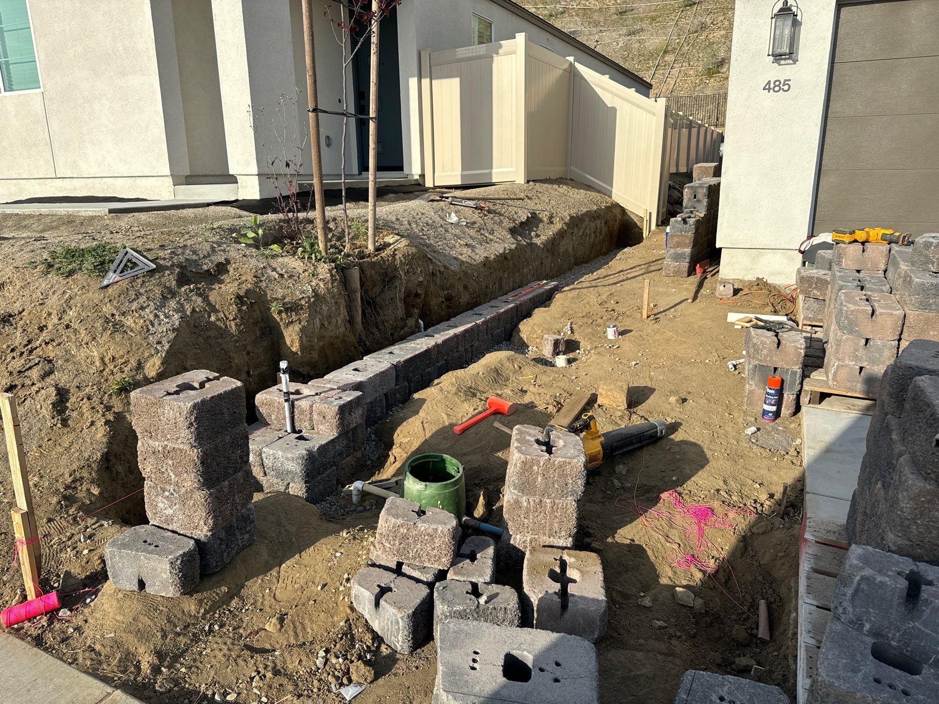 Construction of a retaining wall using gray blocks in front of a house.