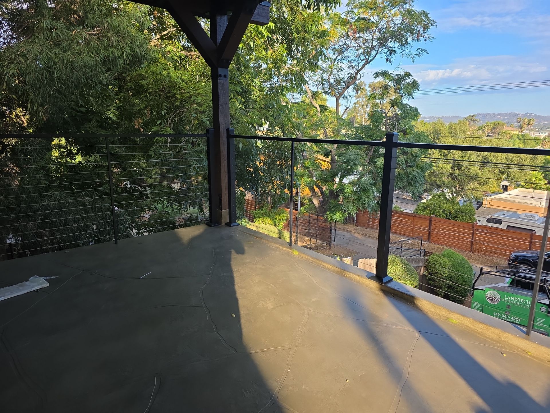 Deck with glass railing overlooking trees and a residential street.