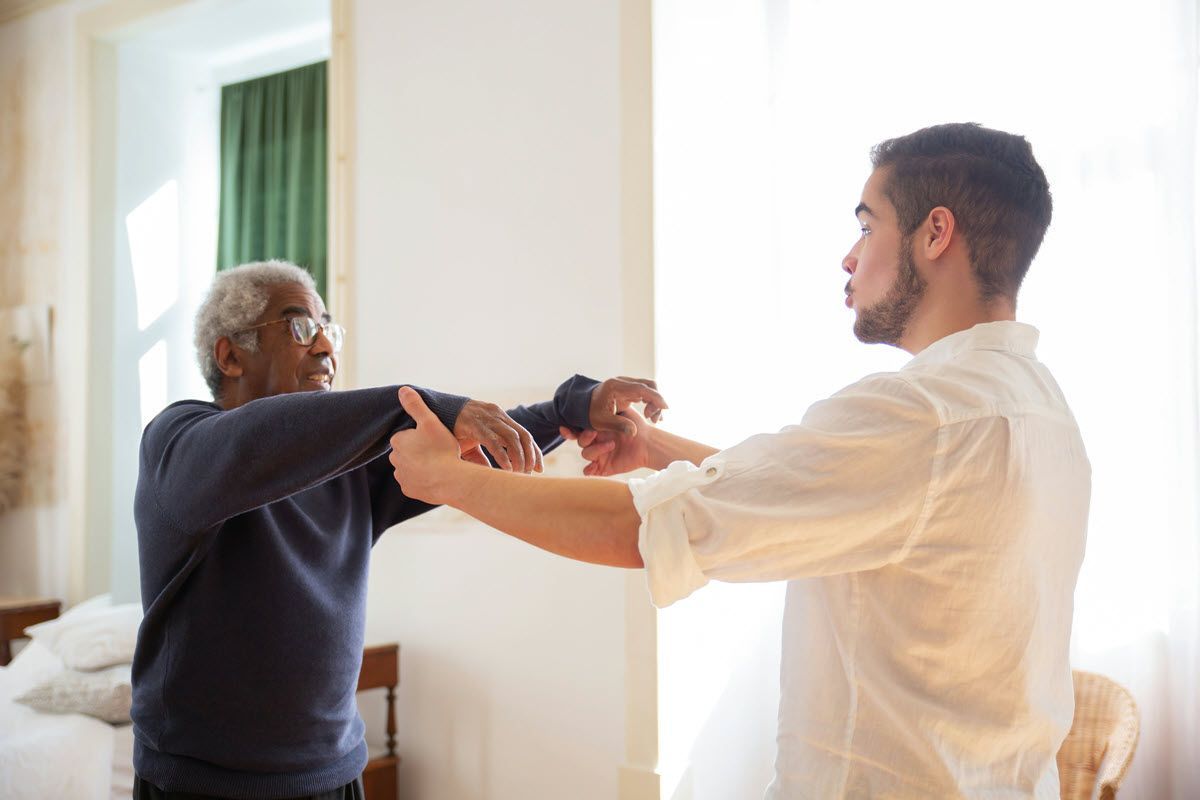 Man helping another man with arm exercises in a bright room.