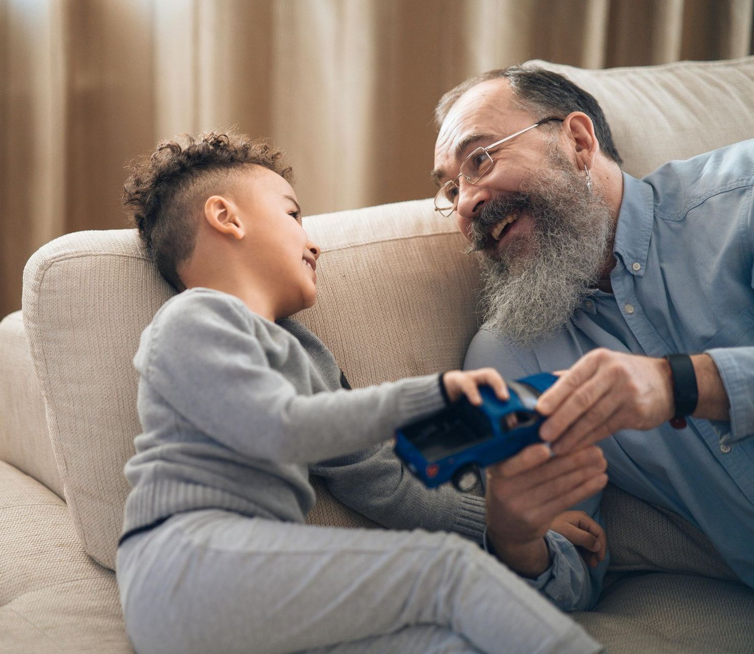 Young child and older person smile, sharing a toy car on a couch.