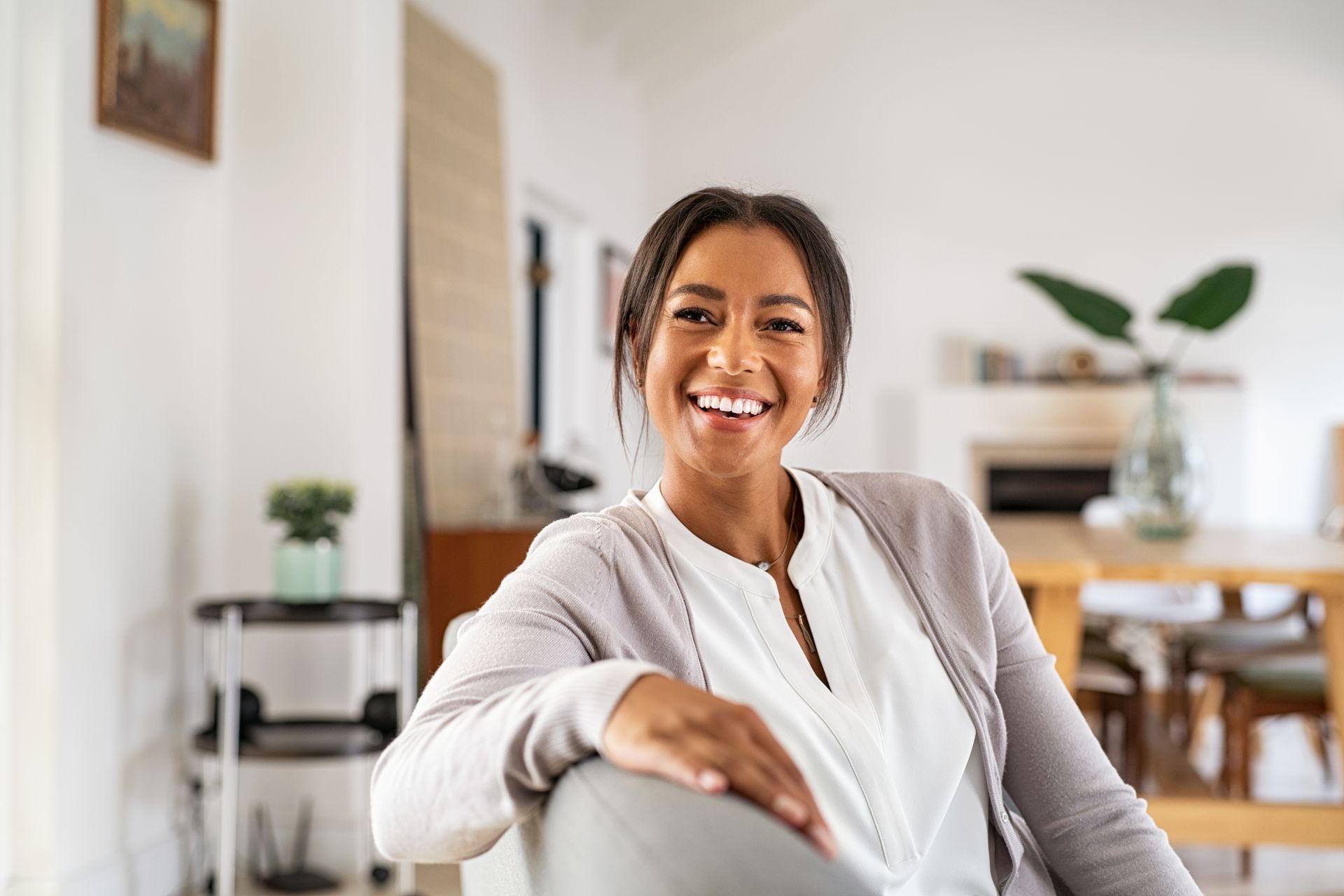Woman smiling in a bright, modern living room, wearing a light cardigan.