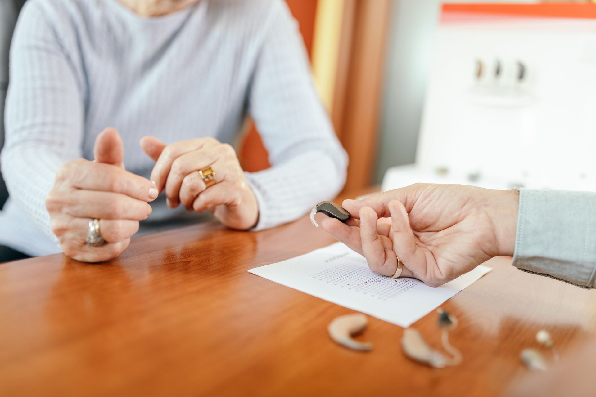 Person holding a hearing aid over a document, as another person gestures.