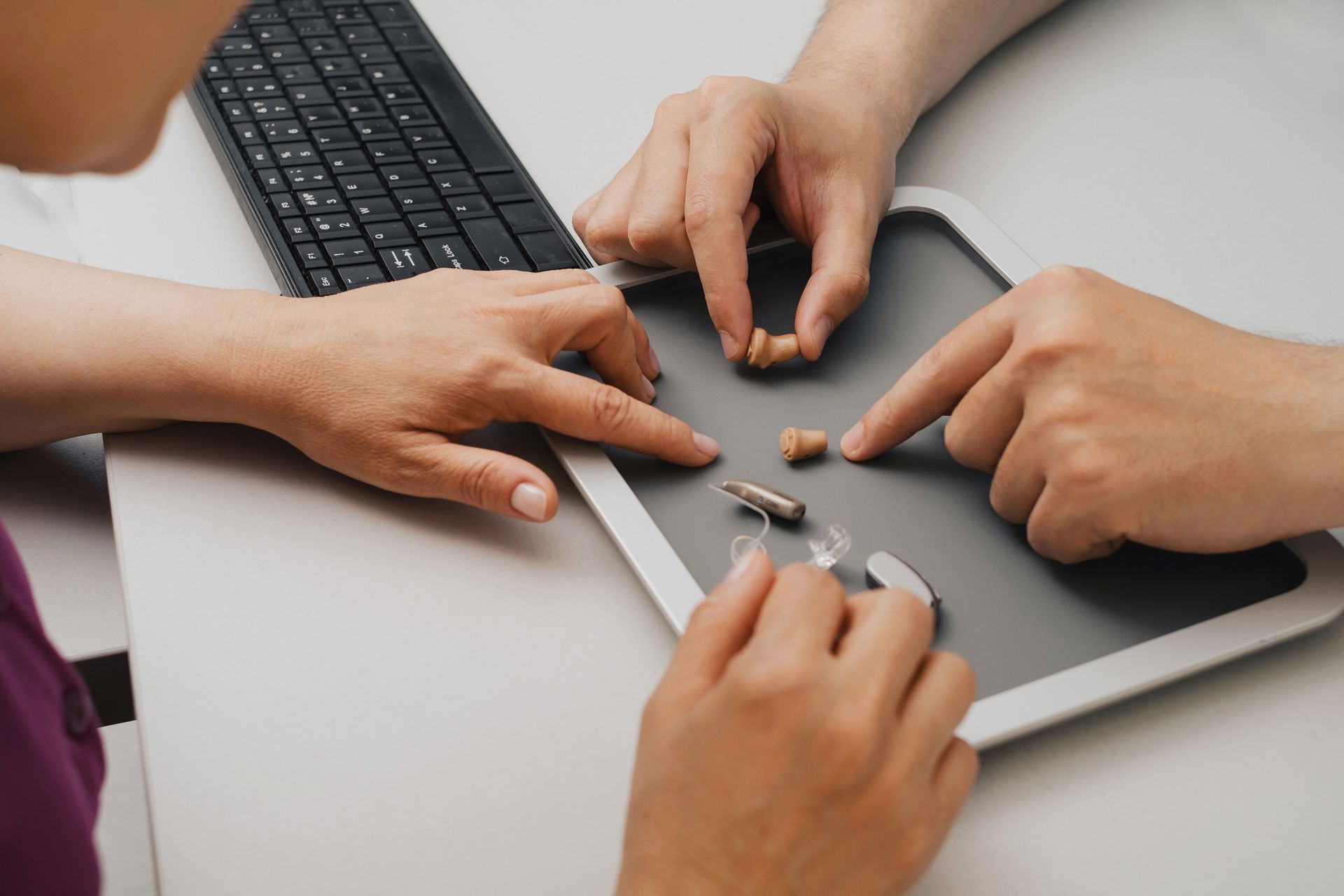 Three people examining different hearing aids on a gray surface.