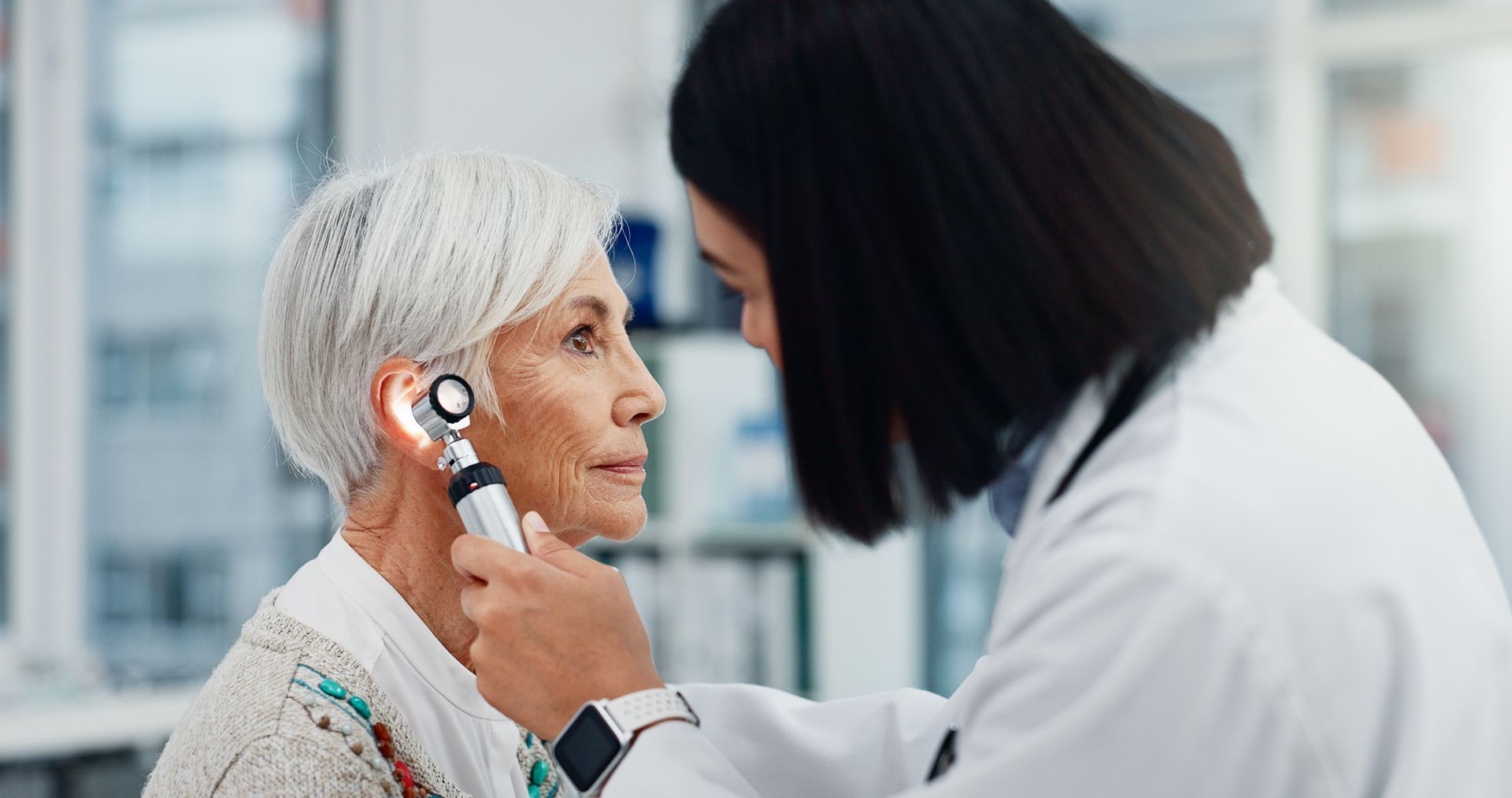 A doctor examines a patient's ear with an otoscope in a medical setting.
