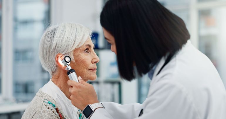 A doctor examines a patient's ear with an otoscope in a medical setting.