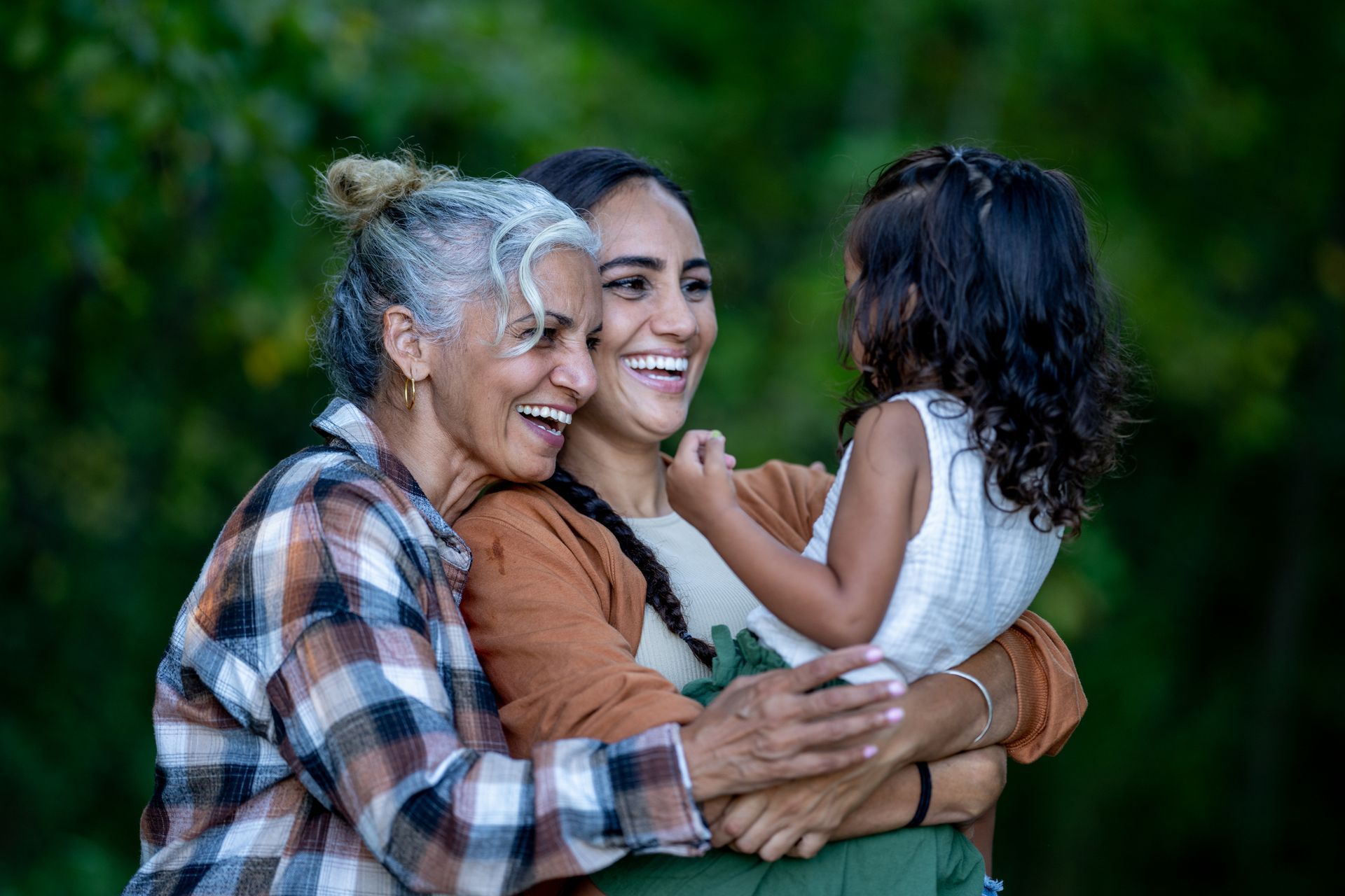 Three people, smiling, embracing outdoors.