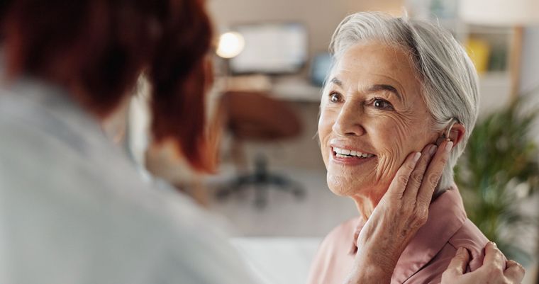 Woman smiles as another person gently touches her face, indoors.