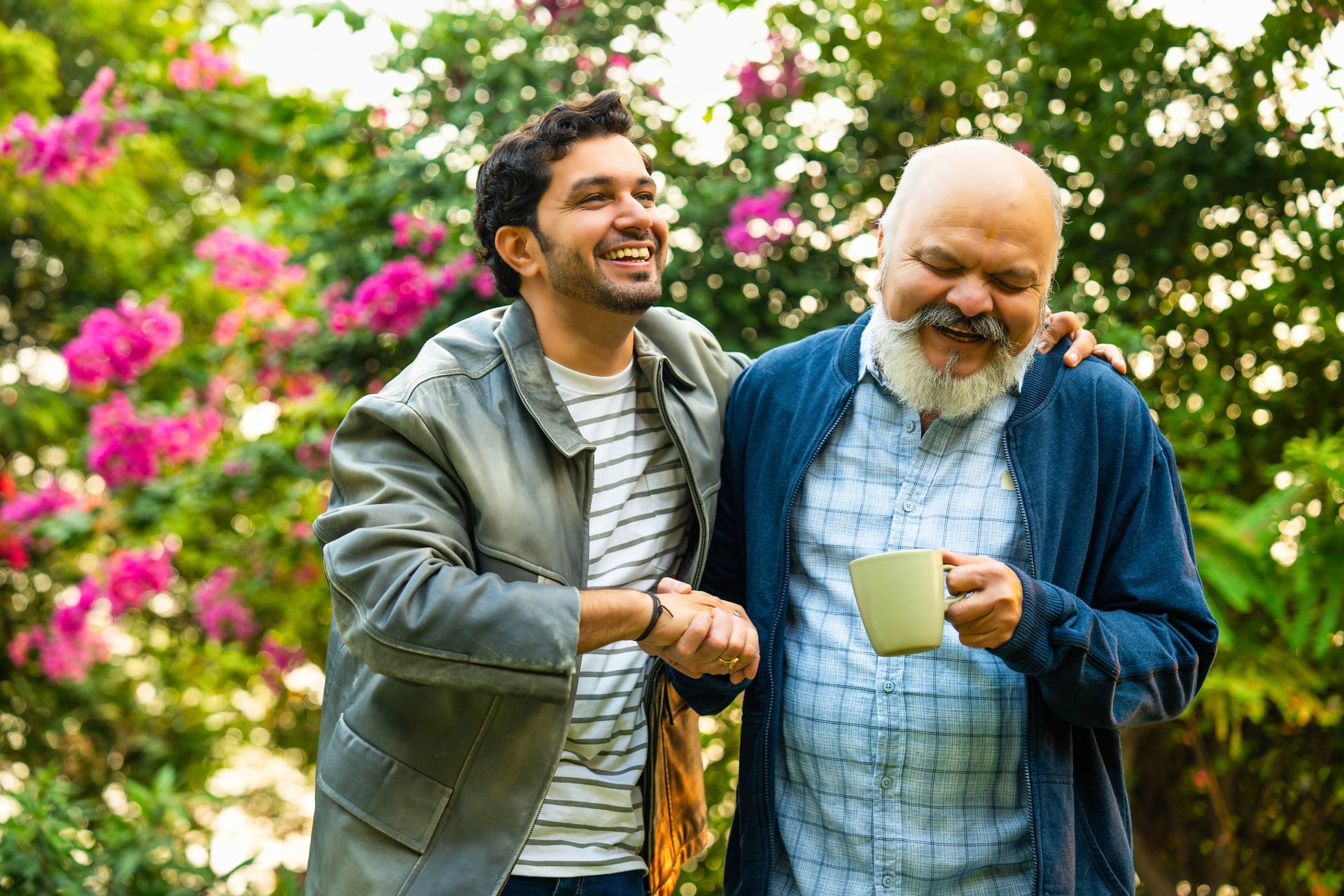 Man with arm around another, both smiling outdoors.