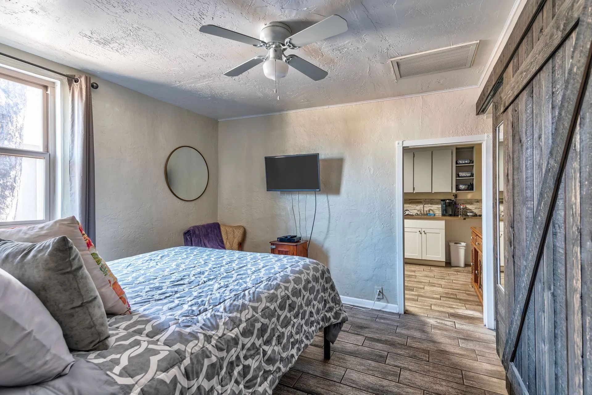 Bedroom with bed, TV, open doorway to kitchen, and rustic sliding door.