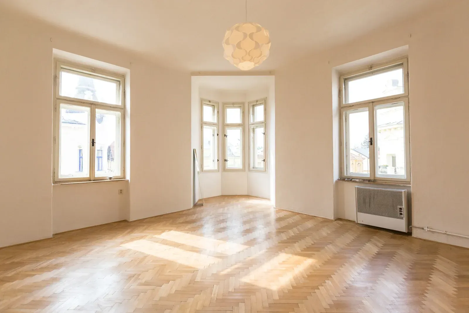 Empty room with parquet floor, three windows, and a round light fixture.