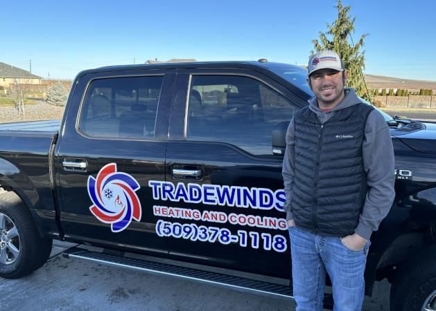 A man is standing in front of a truck that says tradewinds heating and cooling