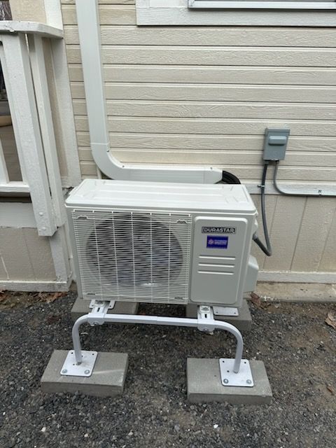 A white air conditioner is attached to the side of a house.