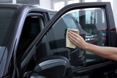 A person is cleaning a car window with a cloth.