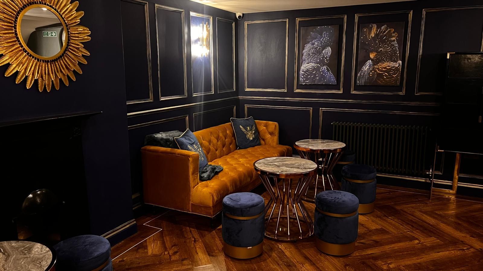 Cozy, dark-walled room with a golden sofa, ornate mirror, and circular tables.