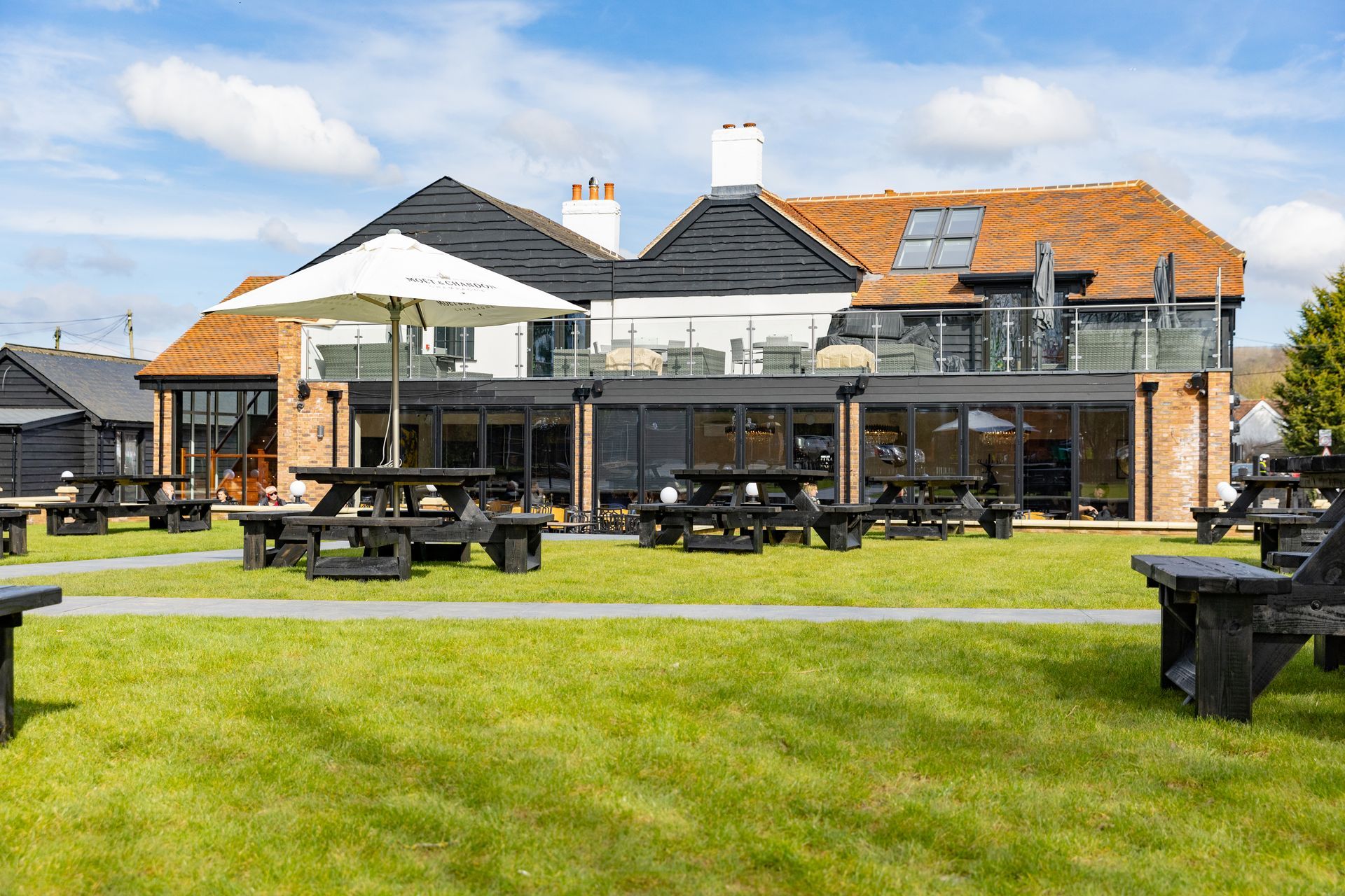 Exterior of a building with a large grassy yard and picnic tables under a sunny sky.