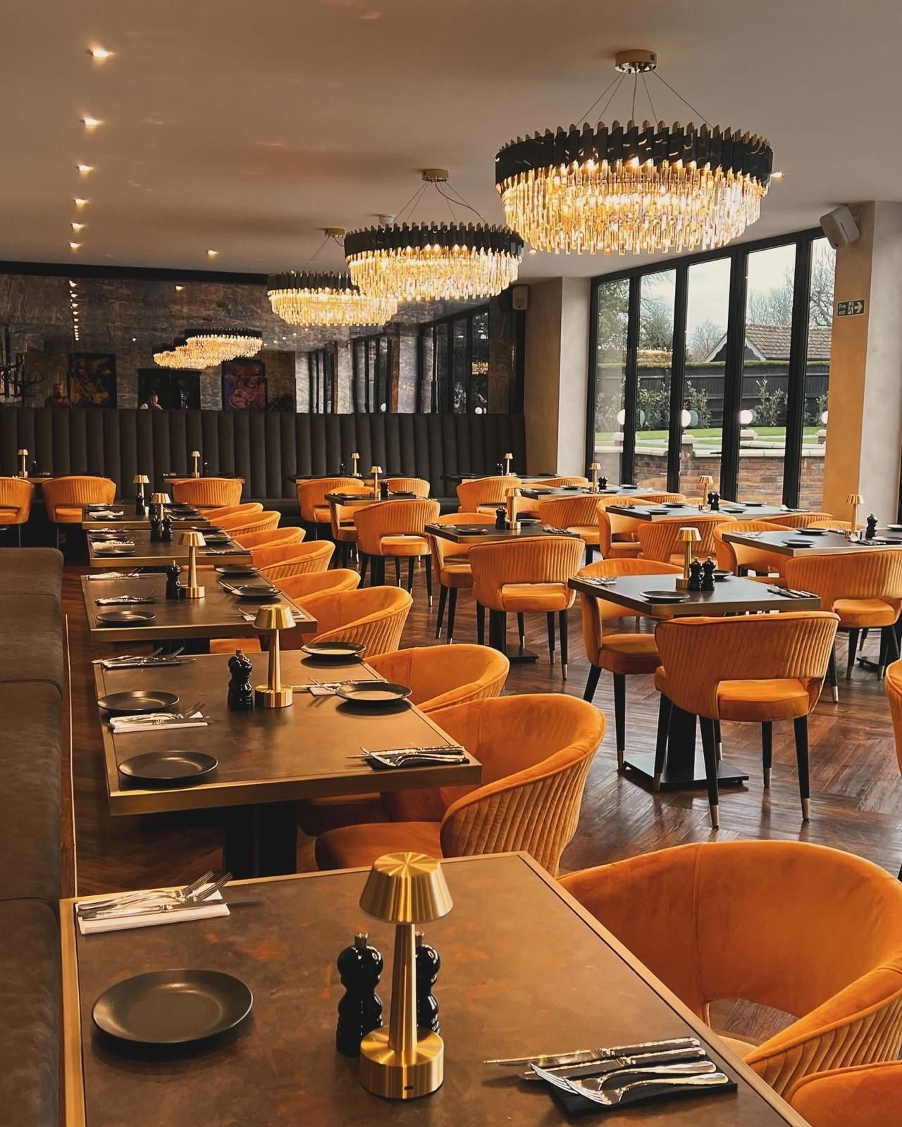 Interior of a restaurant with orange chairs, dark tables, and crystal chandeliers.