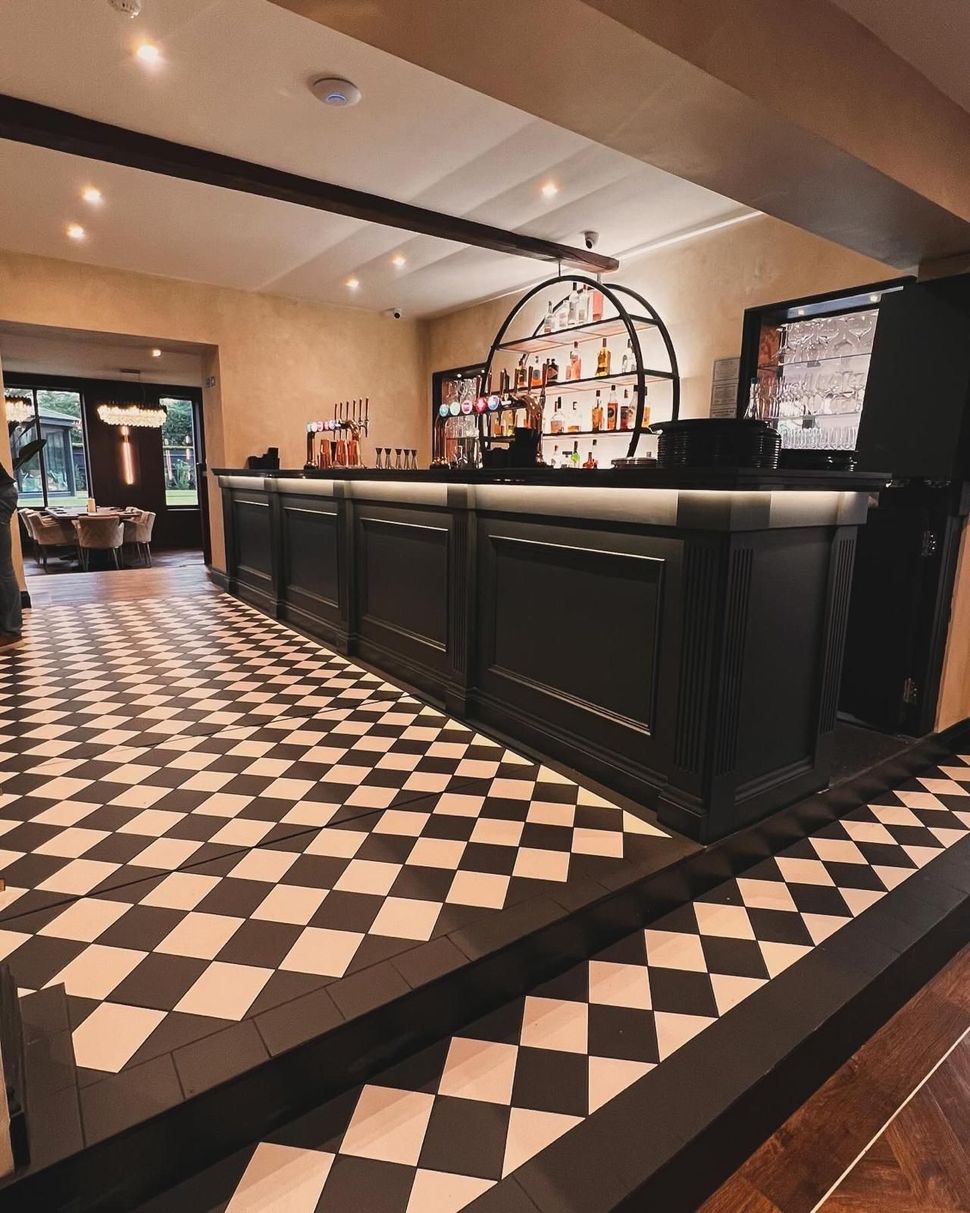 Playground with swings and a wooden playhouse in a pub garden on a cloudy day.