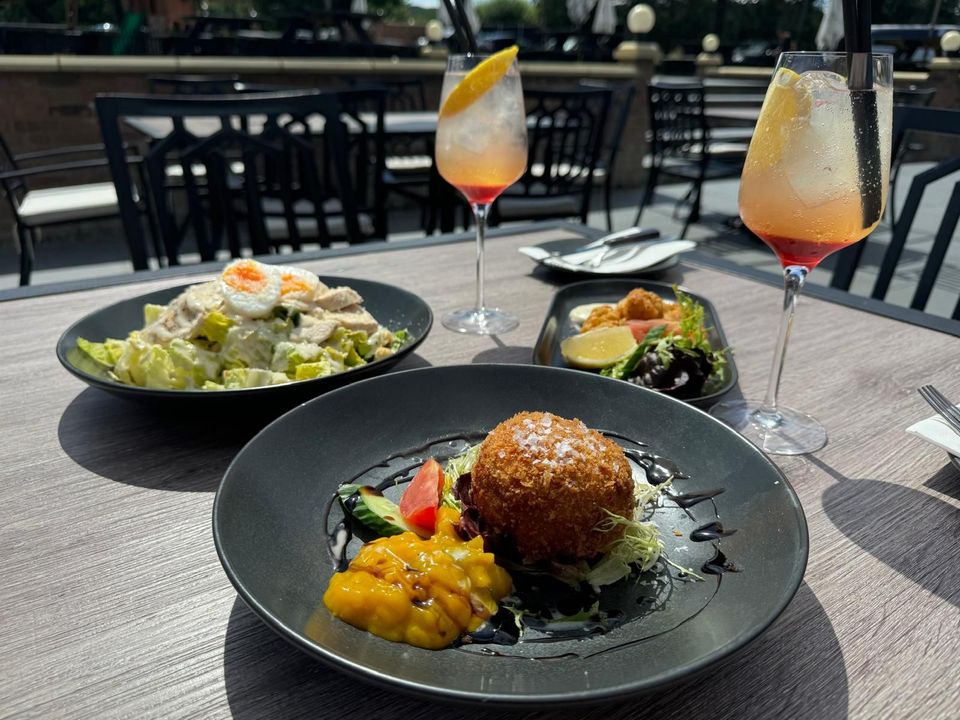 Table with a meal of salad, fried food, and two cocktails in outdoor dining setting.