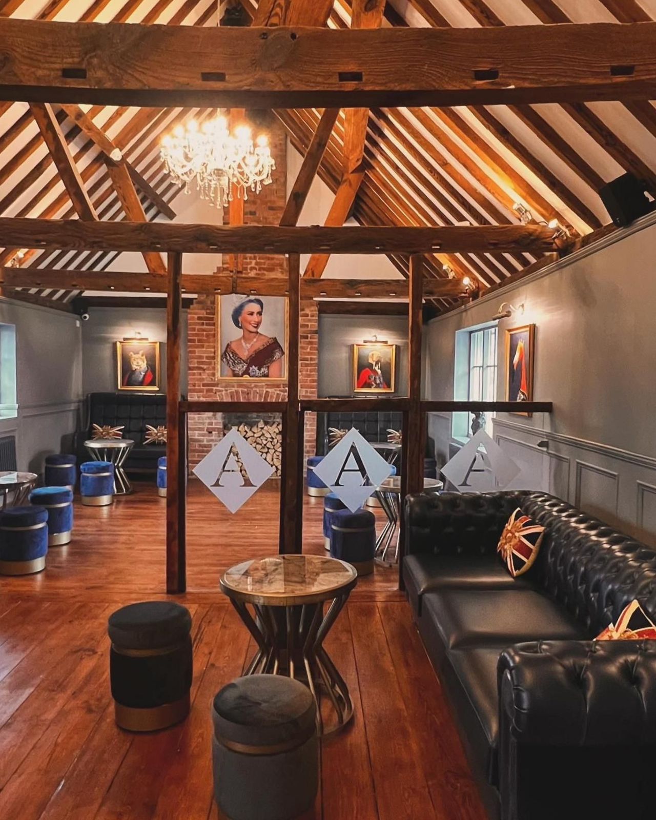 Interior view of a venue with wood beams, portraits, and a black leather sofa with a Union Jack pillow.
