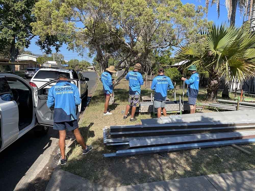 A Group Of Men Are Standing Next To Each Other In Front Of A Car — Posty’s Roofing In Airlie Beach, QLD