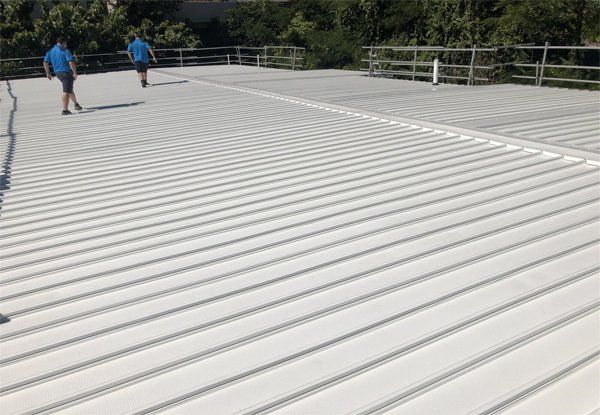 Two Men Are Standing On Top Of A White Roof — Posty’s Roofing In Airlie Beach, QLD