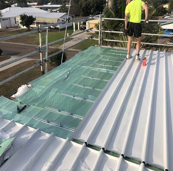 A Man Is Standing On Top Of A White Metal Roof — Posty’s Roofing In Airlie Beach, QLD