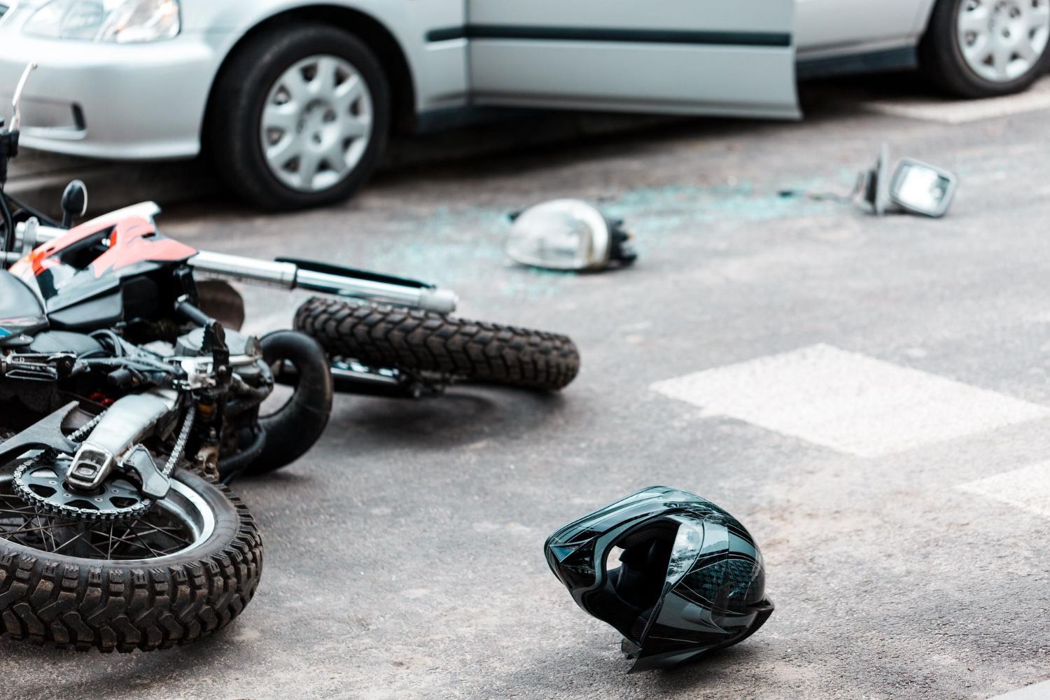 Motorcycle crash scene with fallen bikes and helmets on a road near a white car