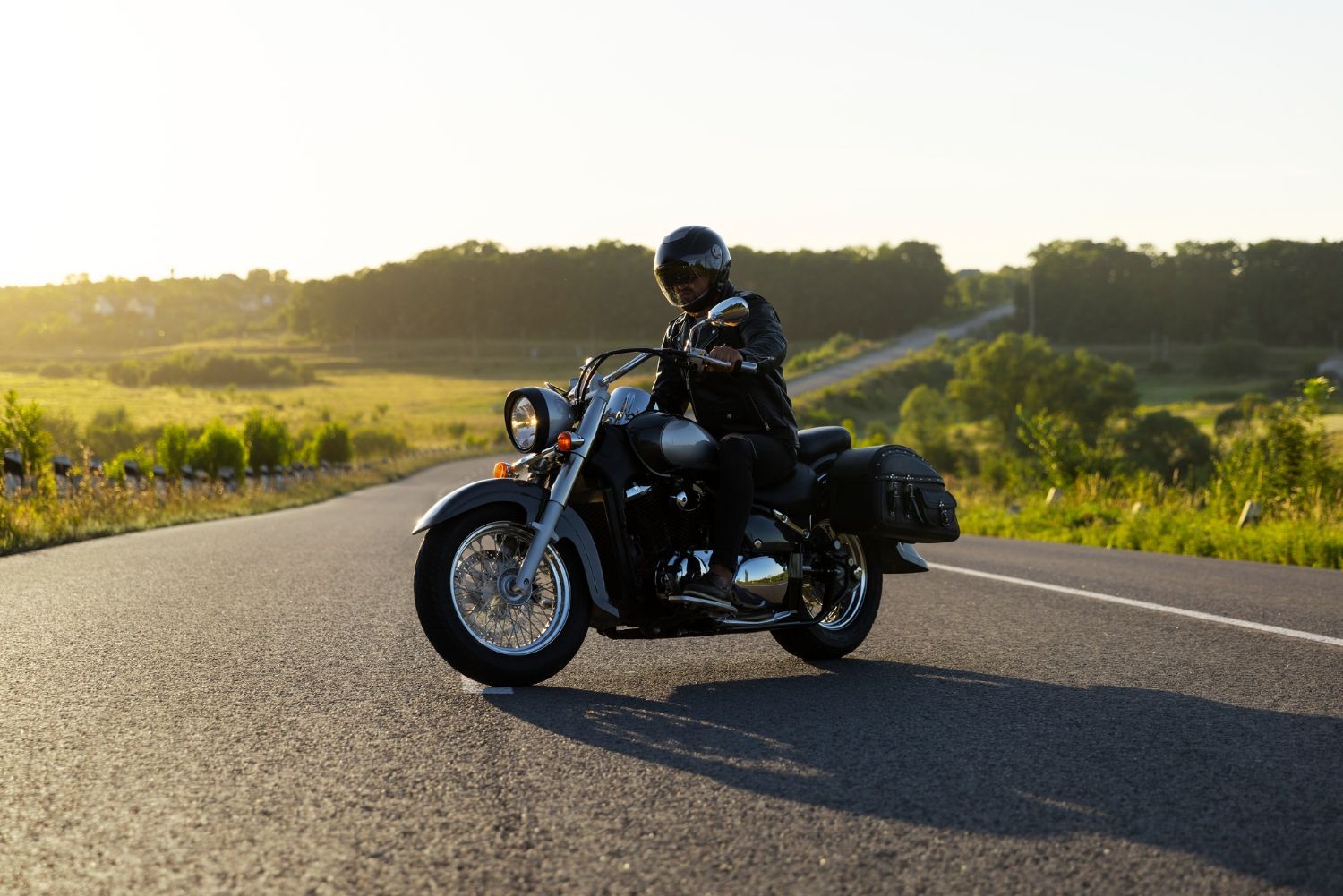 Motorcyclist on a black bike riding along a sunlit rural road at sunset