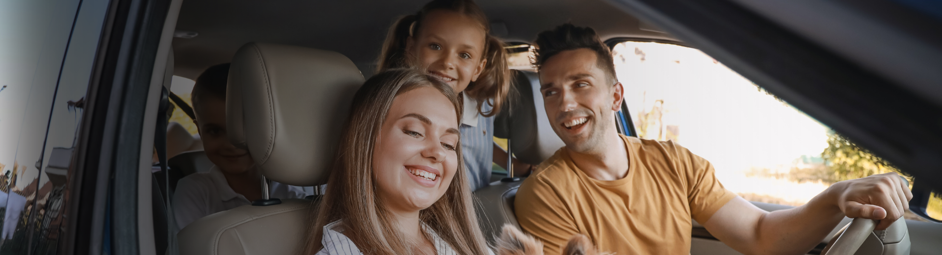 Família sorrindo no carro. Pai dirigindo, mãe e filha no banco de trás. Cores quentes, dia ensolarado.