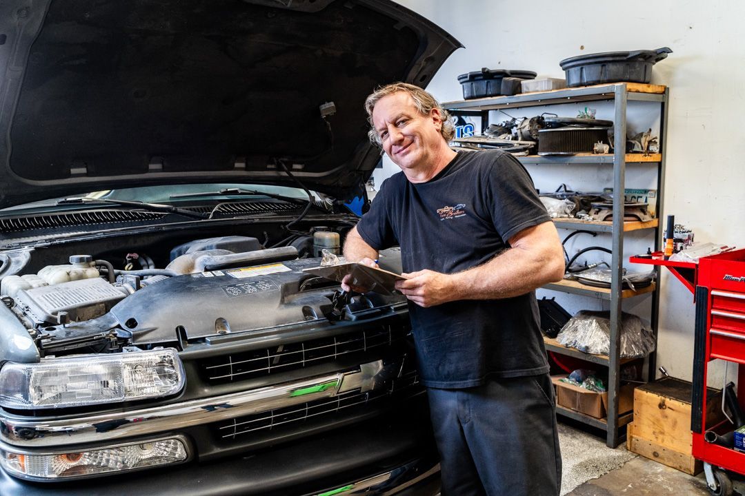 A man is standing next to a truck with the hood up in a garage.