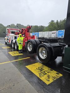 A man is standing next to a tow truck in the rain.