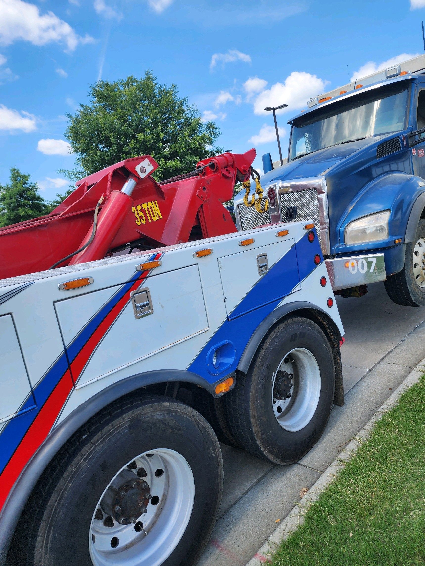A red white and blue tow truck is parked next to a blue truck.