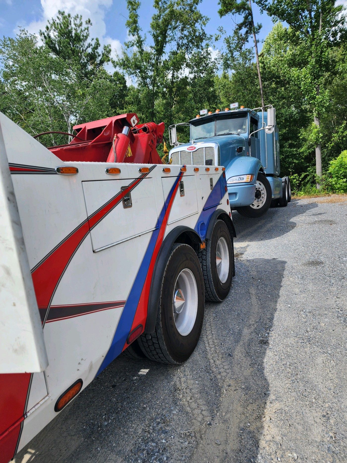 A red white and blue tow truck is parked next to a blue semi truck.