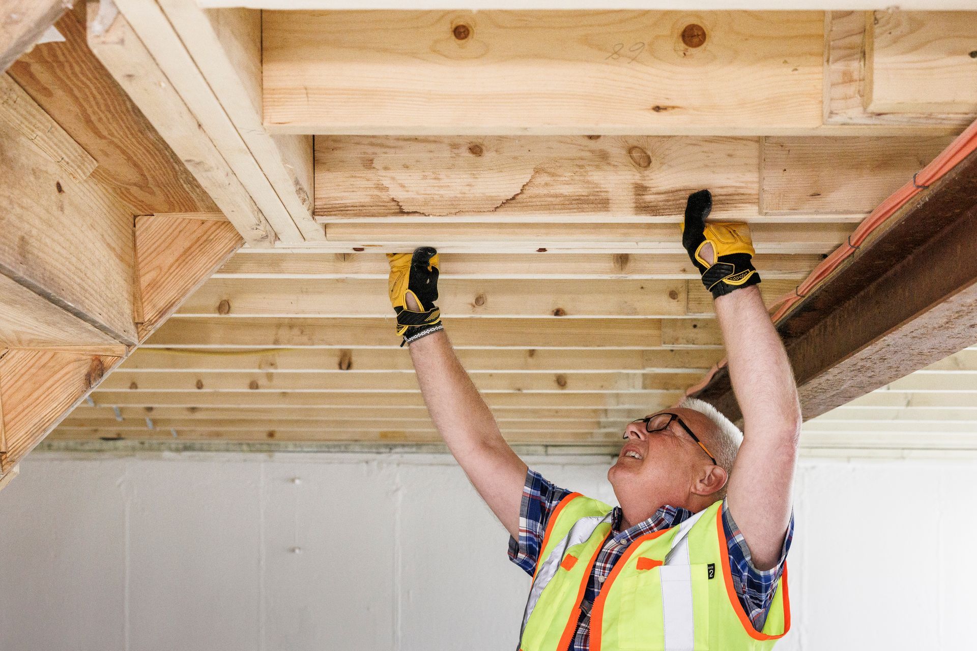 APEX Design Build works on a basement remodeling project in Maplewood, MN, with a worker adjusting wooden ceiling beams