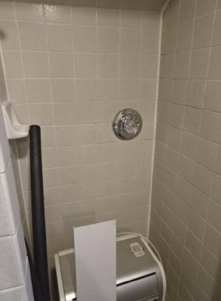 Small shower with beige tiles, a showerhead, and a small appliance.