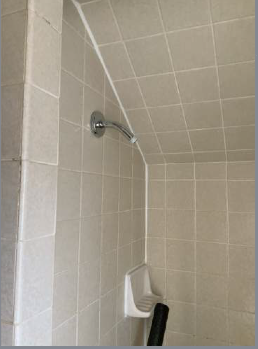 Beige tiled shower with silver showerhead and soap dish. Angled ceiling.
