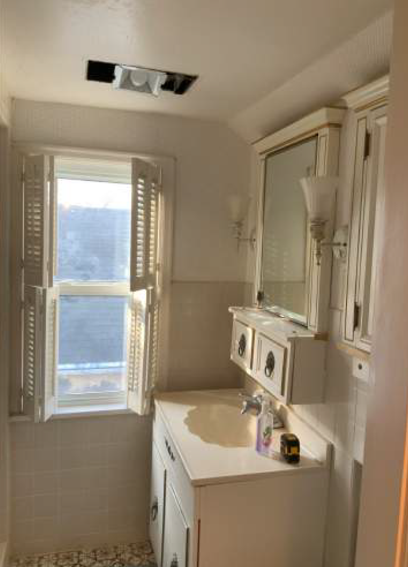 Bathroom interior with a window, vanity, mirror, and medicine cabinet, white cabinets, and a vent in the ceiling.