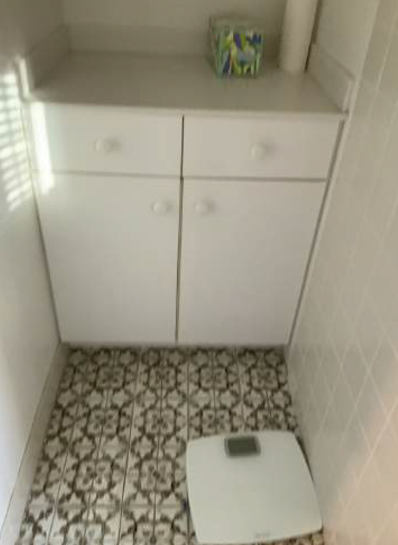 White cabinet above patterned tile floor with a scale.