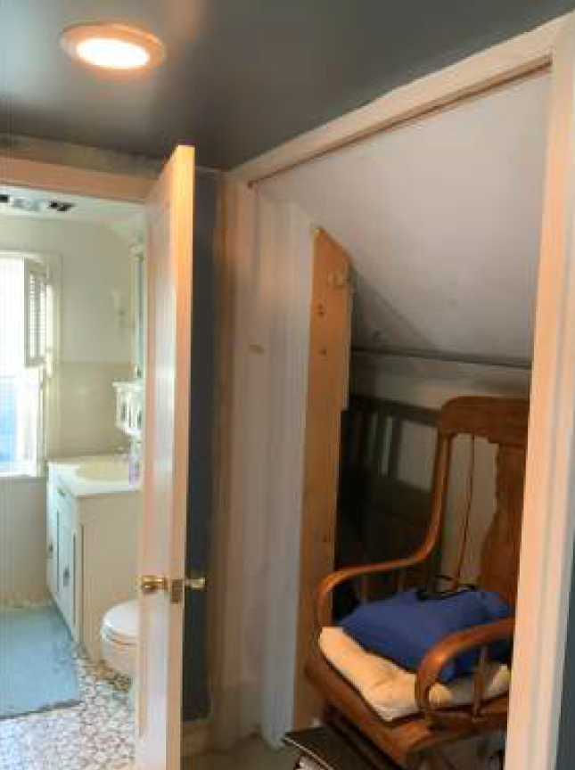 Open doorway reveals a bathroom and a small storage space with a rocking chair.